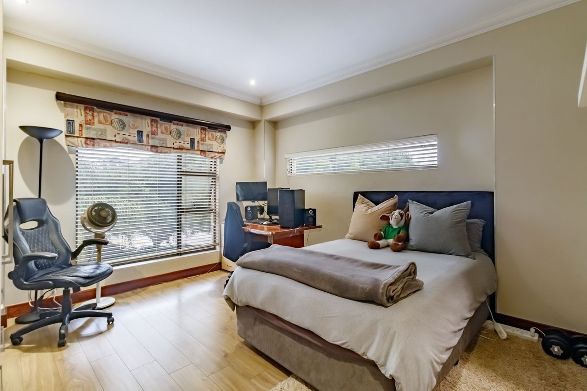 A well-lit bedroom featuring laminate flooring, neutral wall tones, and dual window treatments including venetian blinds.