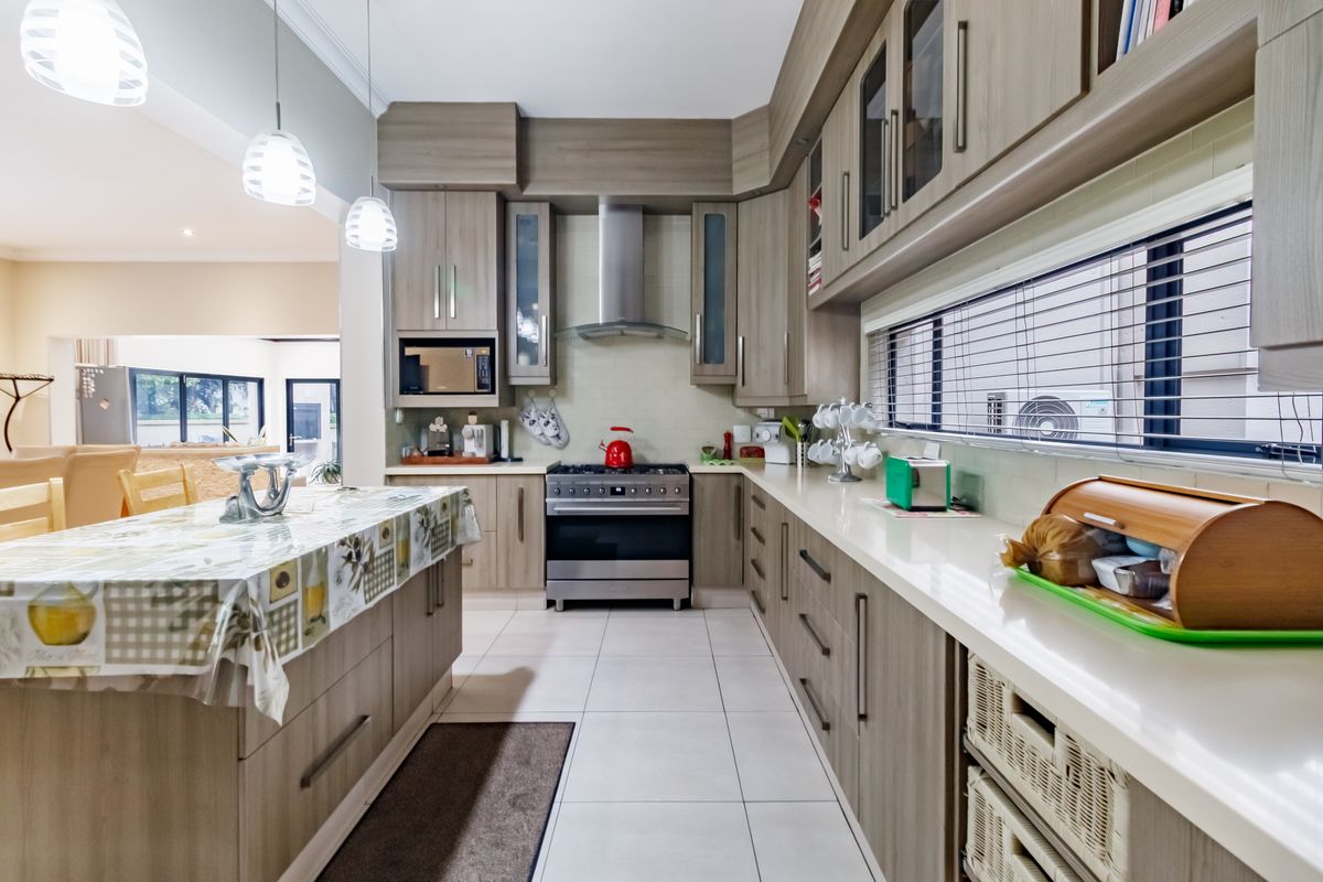 Modern kitchen featuring wood-finish cabinetry, stone countertops, stainless steel appliances, and a central island, seamlessly flowing into the adjacent living area.