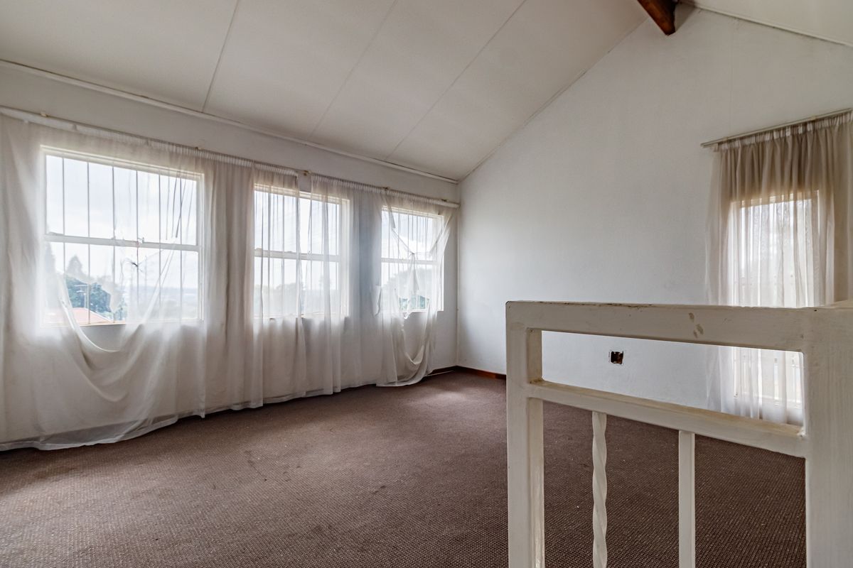 An empty bedroom featuring a vaulted ceiling, large windows with security bars, and a mezzanine-style railing overlooking the lower level.