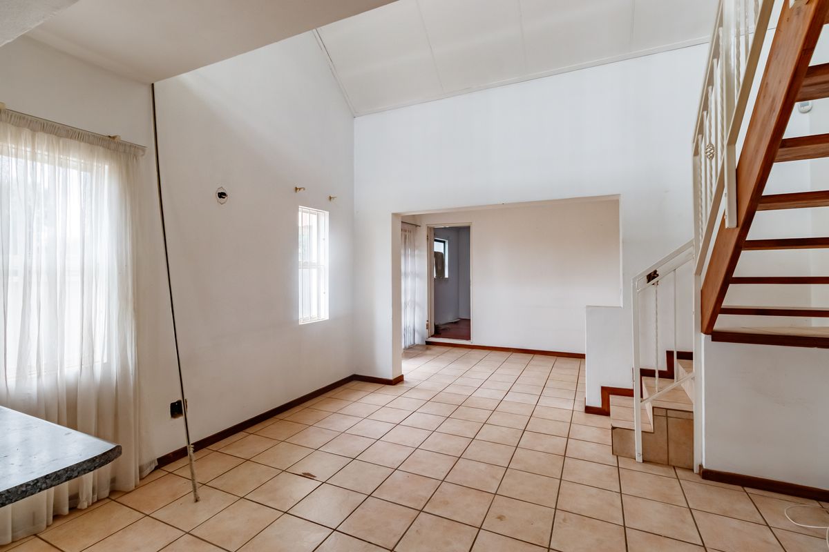 An empty, open-plan living area featuring tiled flooring, a vaulted ceiling, and a staircase with a metal balustrade.