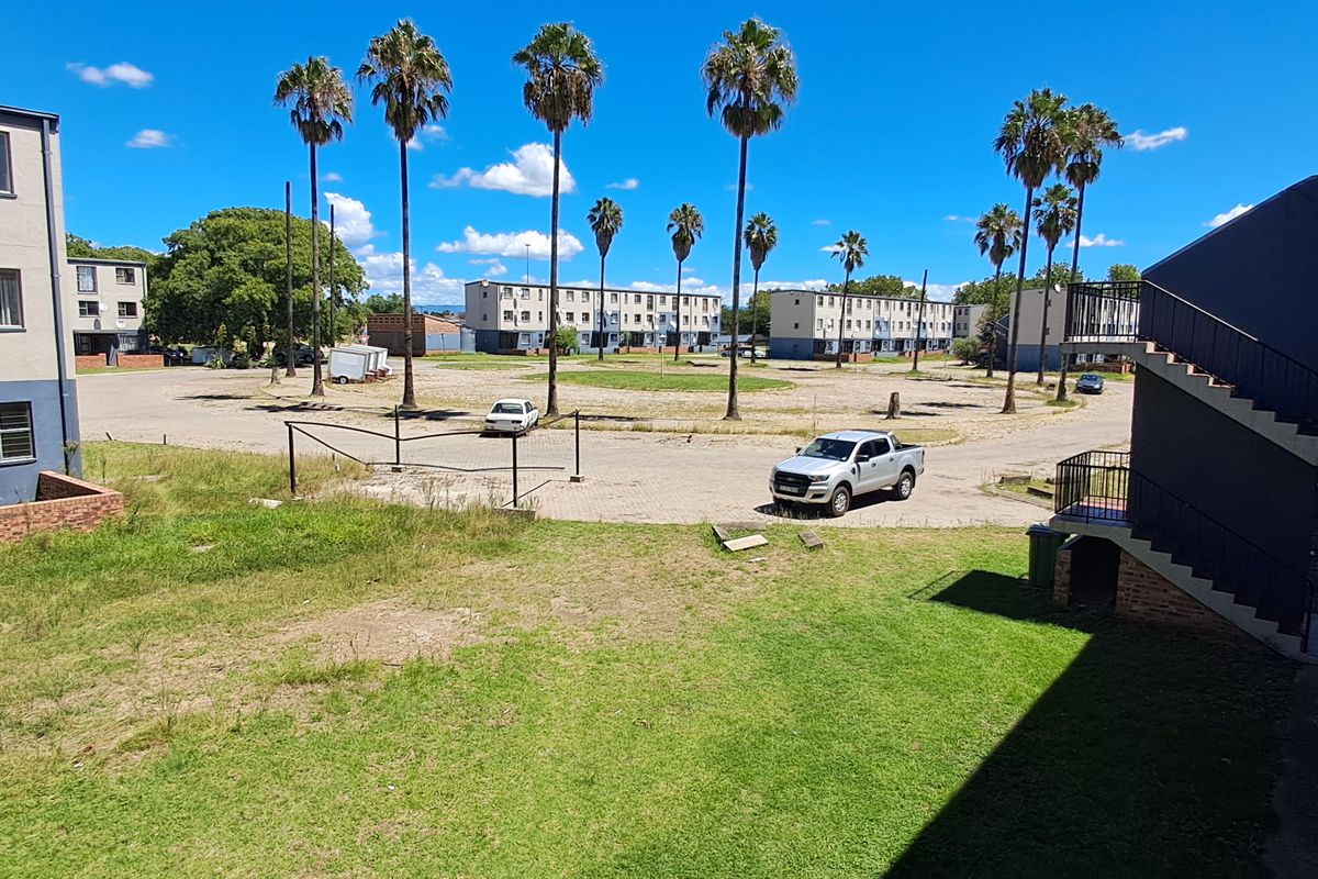 View of the rear exterior area of the flat complex, featuring a communal lawn, paved parking space, and external staircase access.