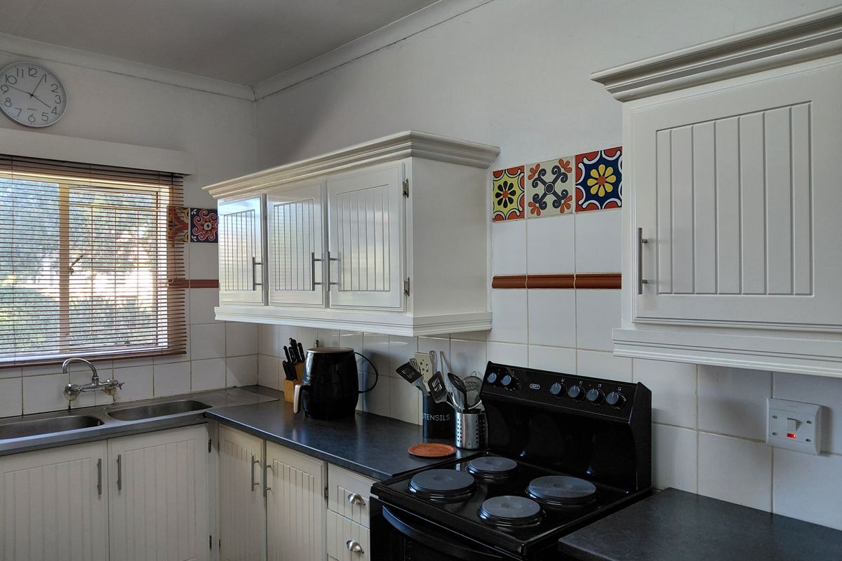 A functional kitchen featuring white cabinetry, a double basin sink, and a black electric stove with decorative tiled backsplash accents.
