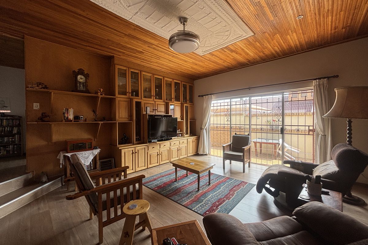 A living room featuring timber panelled ceilings, a decorative ceiling rose, extensive built-in timber cabinetry, and sliding glass doors leading to an outdoor area.