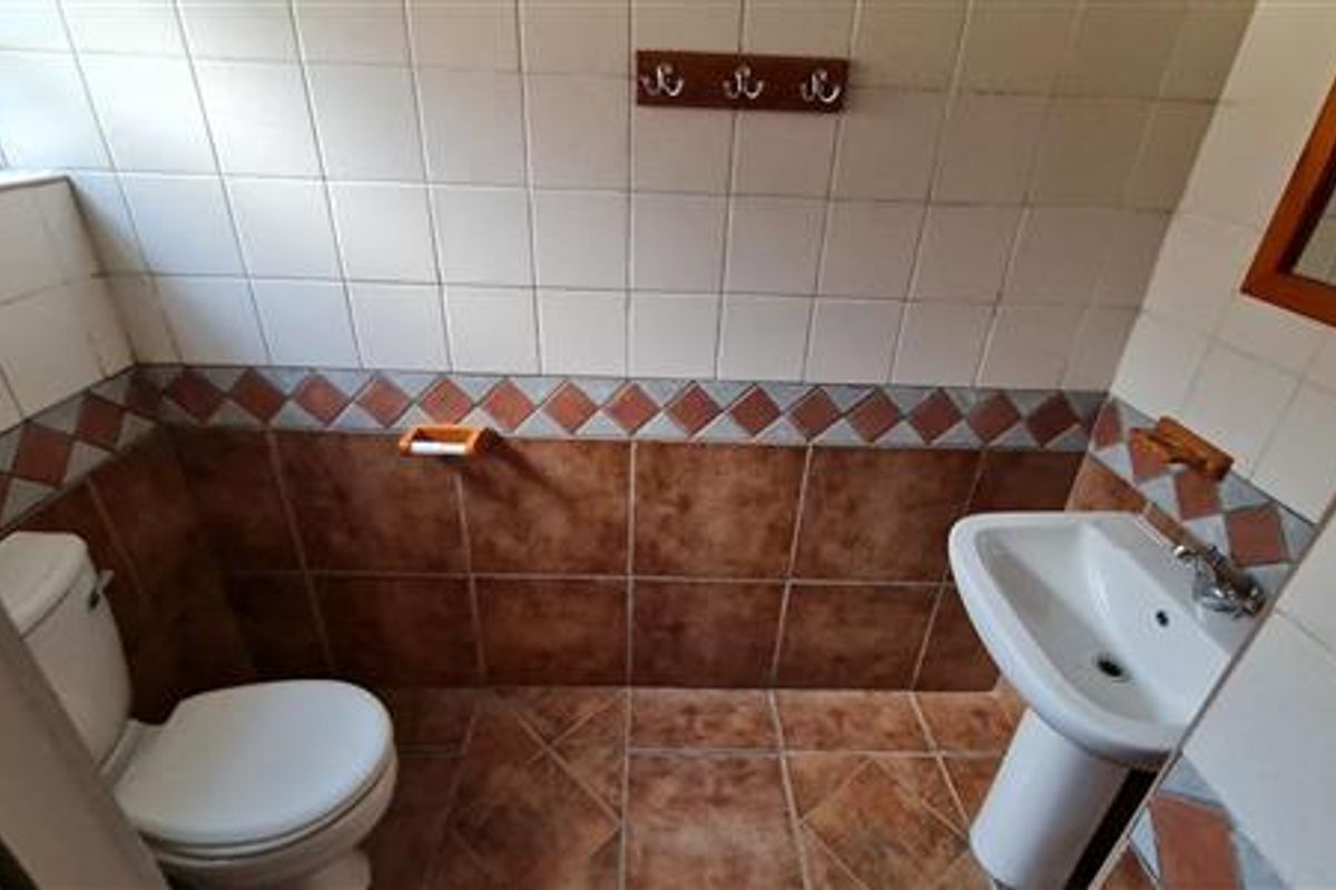 A functional bathroom featuring a pedestal basin, toilet, and classic ceramic wall and floor tiling.