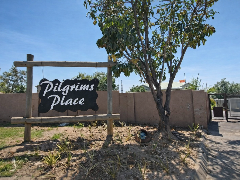 Entrance view of Pilgrims Place featuring a perimeter wall, security gate, and electric fencing.
