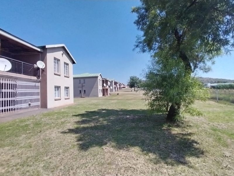 Exterior view of the apartment complex featuring multi-story units with balconies, security gates, and surrounding communal lawn areas.