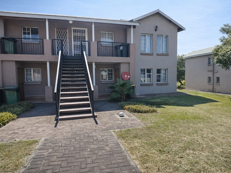 Exterior view of a two-story apartment building featuring a central metal staircase, paved walkway, and balcony access.