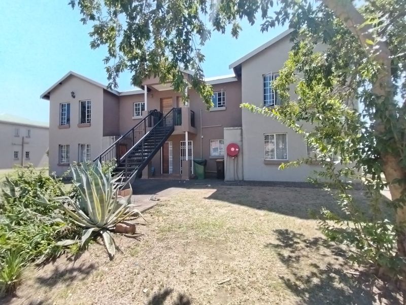 Rear view of the apartment complex featuring a metal staircase, security gates, and a fire hose reel with surrounding garden area.