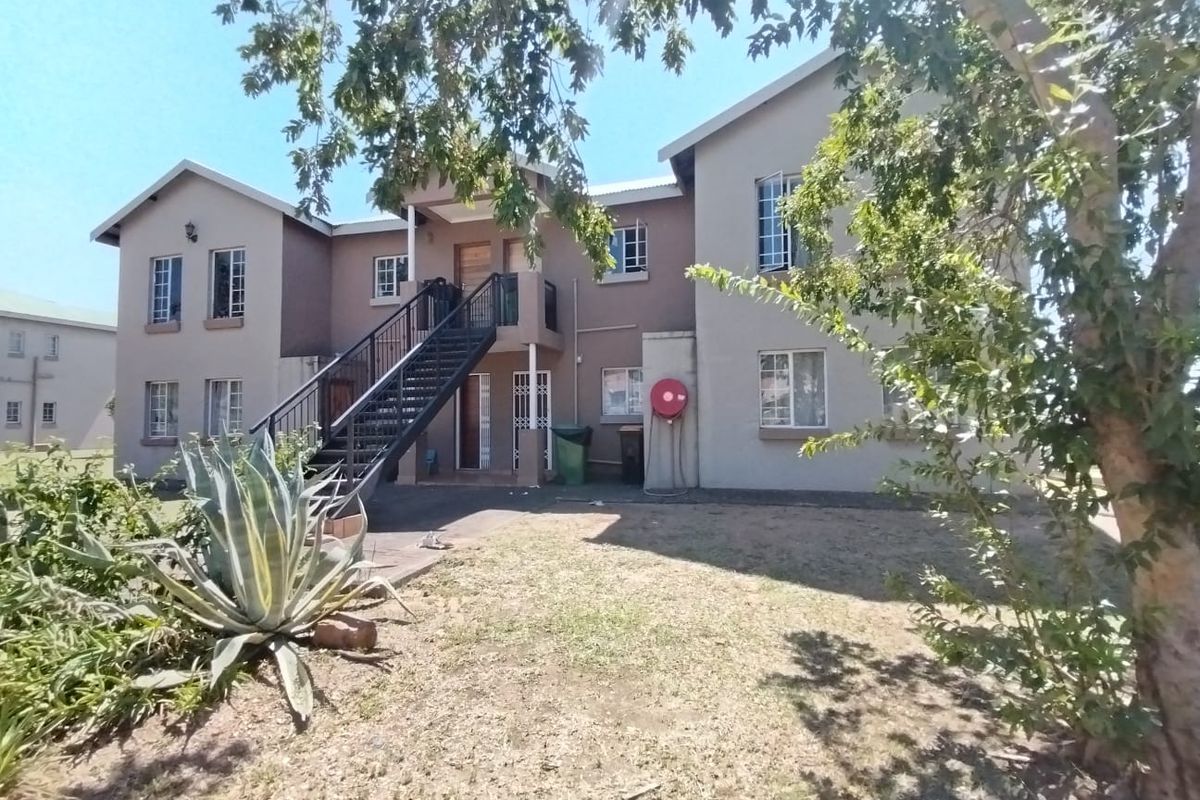 Rear view of a multi-story apartment building featuring a metal external staircase, security gates, and a shared garden area.