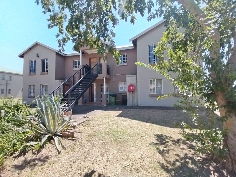 Rear view of a multi-story apartment building featuring a metal external staircase, security gates, and a shared garden area.