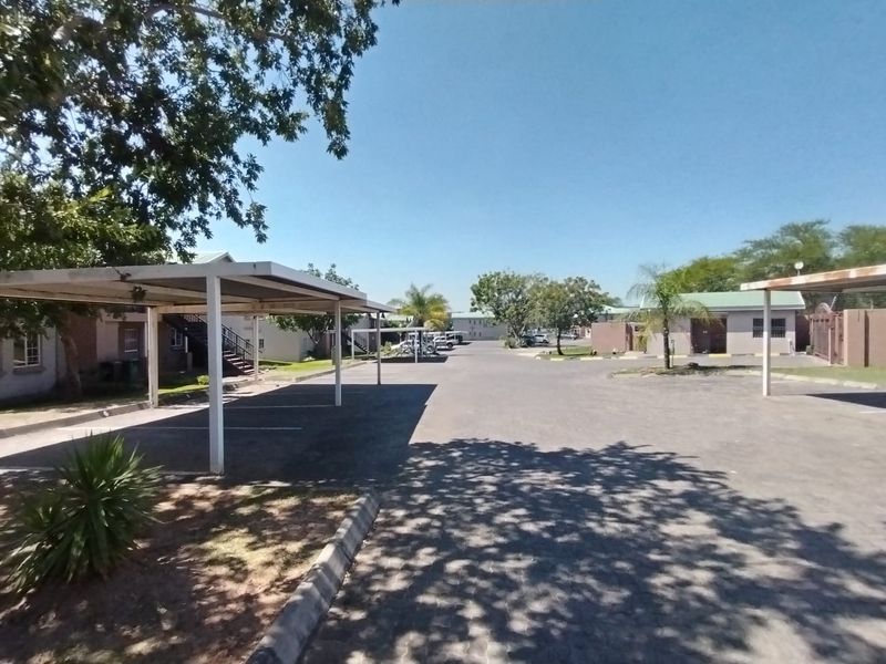 An exterior view of the apartment complex featuring covered parking bays, paved driveways, and established landscaping.