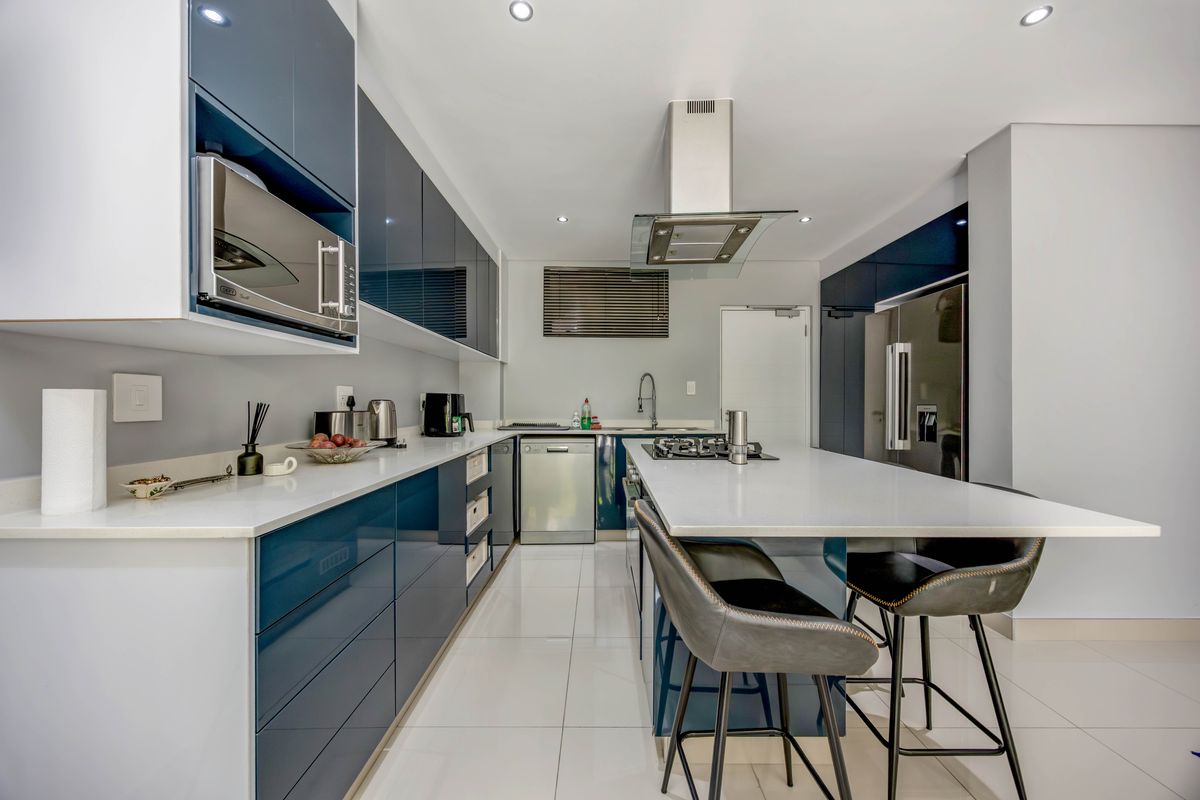 Modern kitchen featuring high-gloss blue cabinetry, stone countertops, a central island with breakfast bar, integrated appliances, and a stainless steel extractor fan.