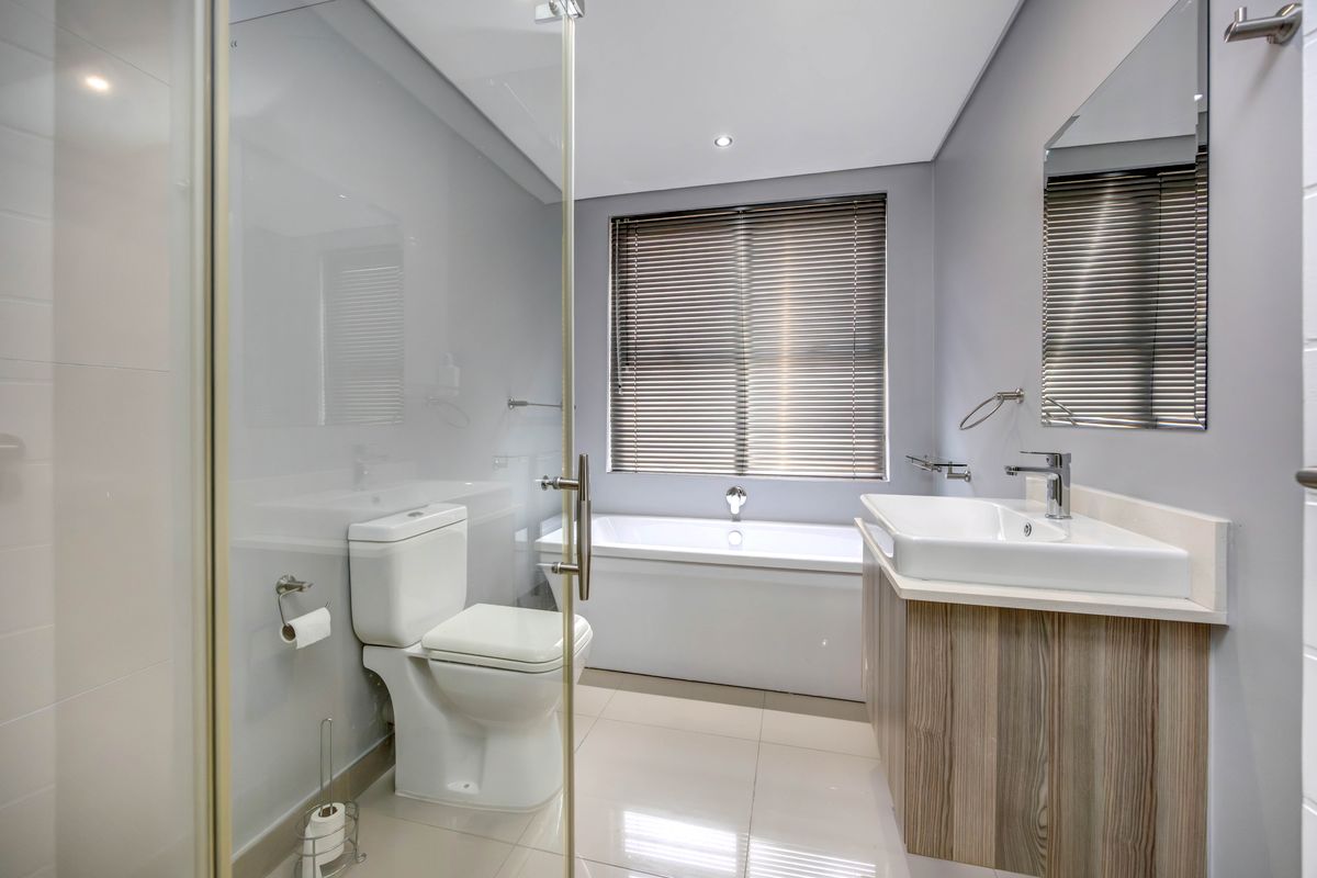 Modern bathroom featuring a sleek vanity, a deep soaking bathtub, and a glass-enclosed shower with contemporary fixtures and neutral tiling.