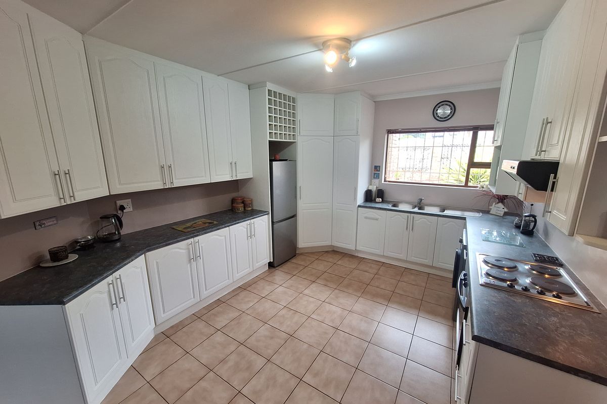 A functional kitchen featuring white cabinetry, dark laminate countertops, tiled flooring, a built-in hob, and an integrated wine rack.