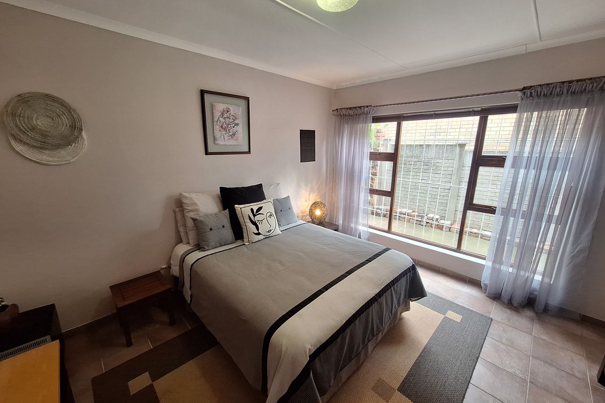 A well-lit bedroom featuring tiled flooring, large windows with security bars, and neutral wall finishes, providing a comfortable and functional living space.