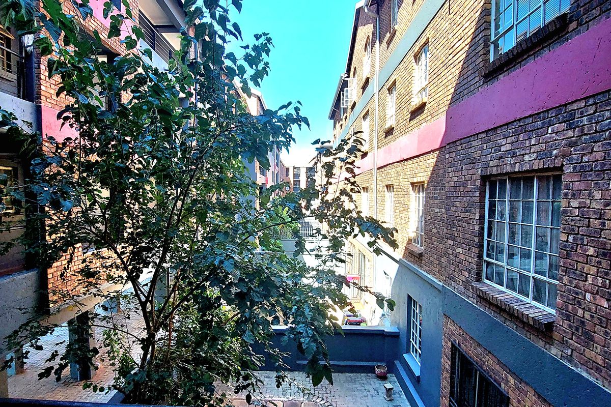 View of a paved courtyard between two multi-story brick townhouse buildings, featuring metal balcony railings and classic multi-pane window frames.