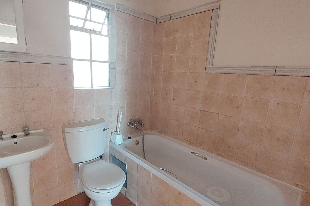 A dated bathroom featuring a pedestal basin, toilet, and bathtub with tiled walls and flooring, offering potential for a modern renovation.