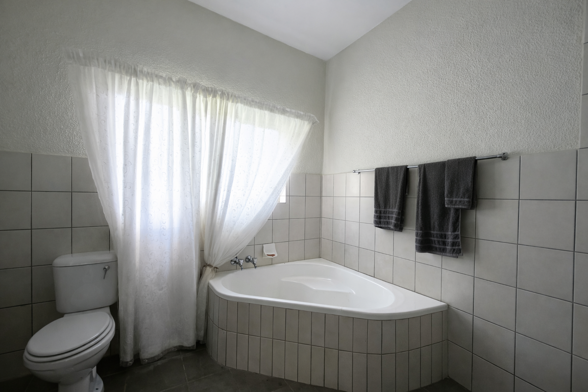 A functional bathroom featuring a corner bathtub, standard toilet, and neutral wall tiling, offering a clean and practical layout.