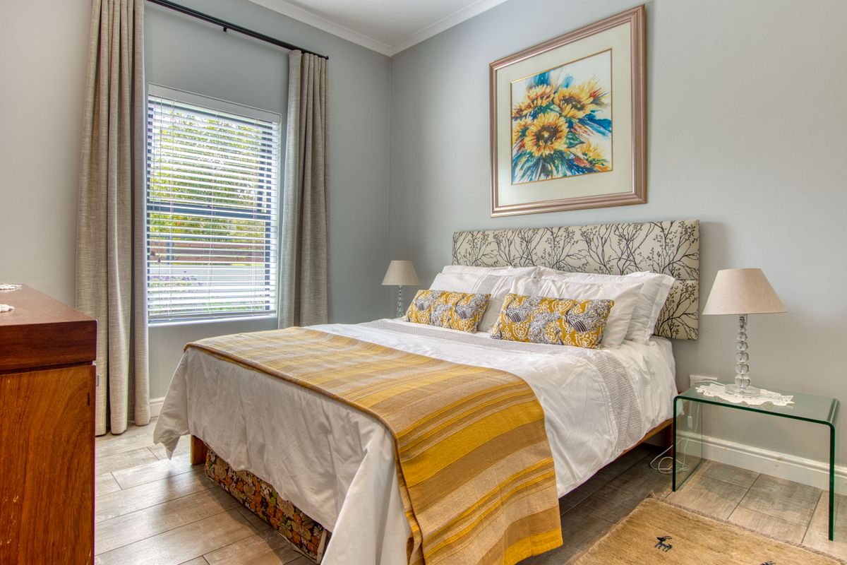 A well-maintained bedroom featuring neutral wall tones, tiled flooring, and a large window with fitted blinds and curtains.