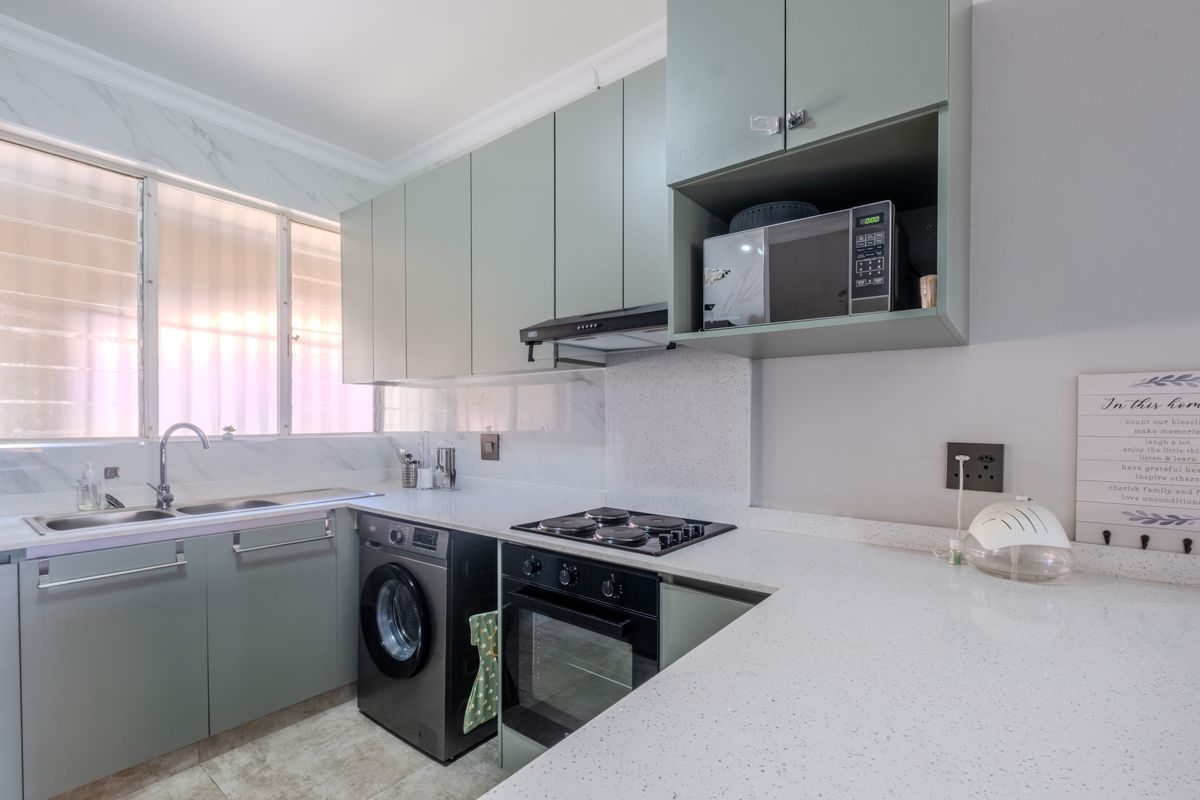 Modern kitchen featuring light green cabinetry, stone countertops, integrated oven, hob, extractor fan, and a built-in space for a washing machine.