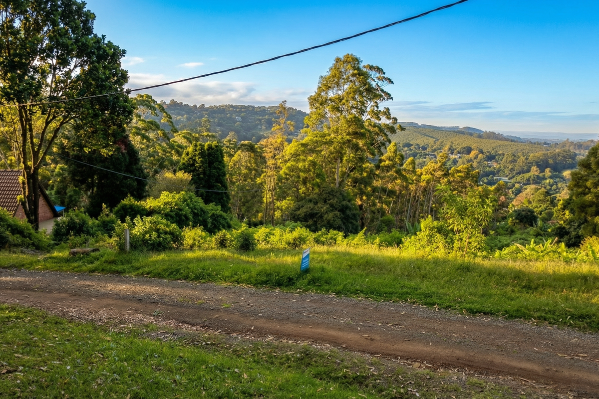 A scenic view overlooking a sloping, tree-lined residential plot with an unpaved access road in the foreground.