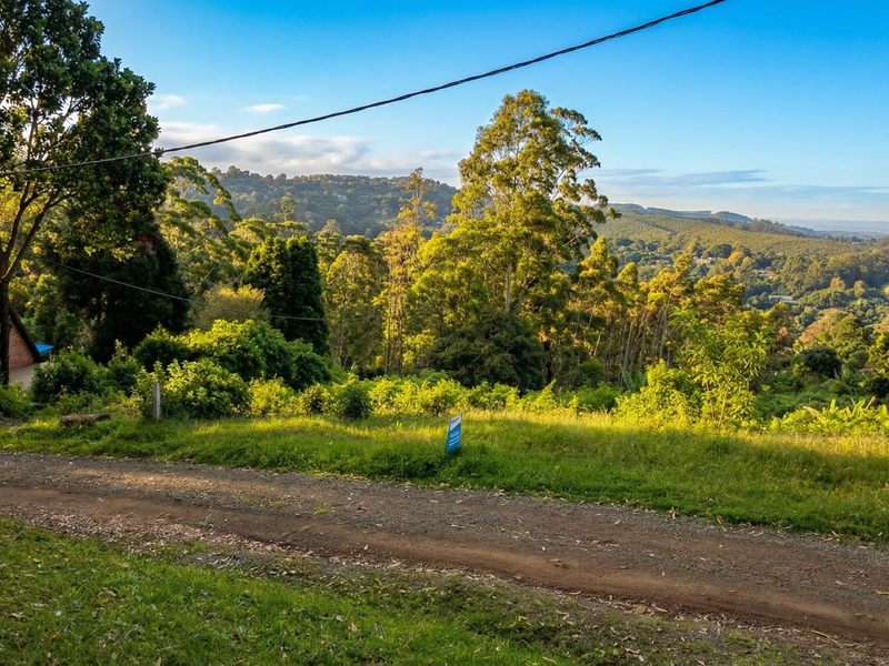 A scenic view overlooking a sloping, tree-lined residential plot with an unpaved access road in the foreground.