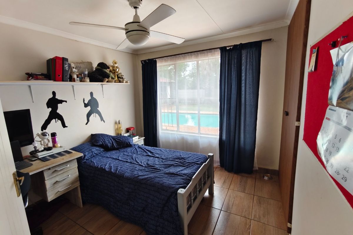 A functional bedroom featuring tiled flooring, a ceiling fan, and a built-in cupboard, with a view overlooking the swimming pool area.