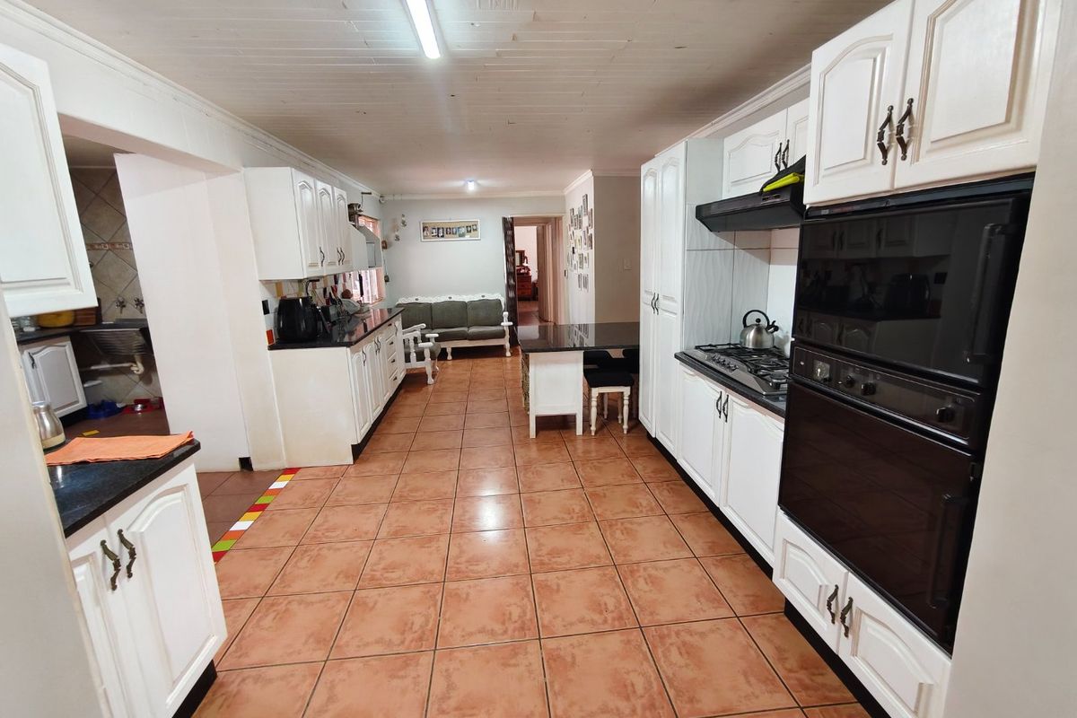 Spacious kitchen featuring white cabinetry, built-in oven, gas hob, and tiled flooring, with an open-plan layout leading to an adjacent living area.