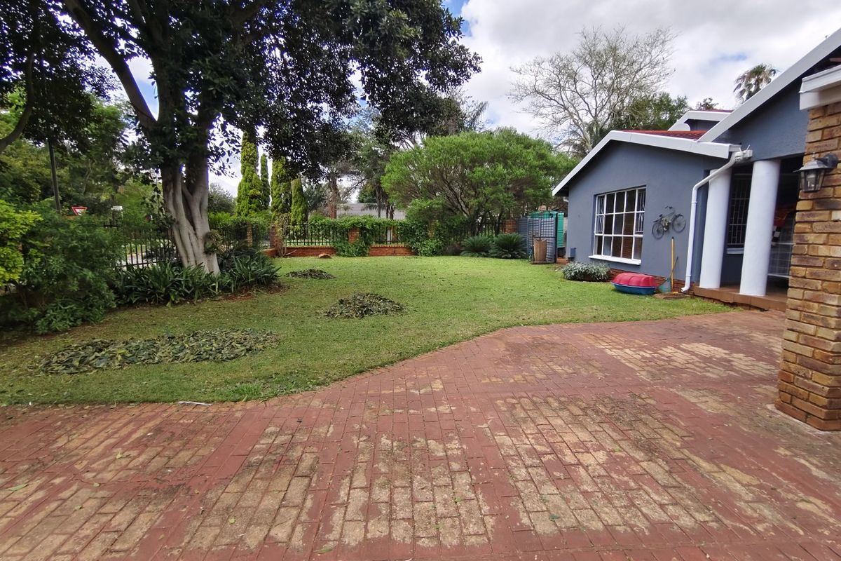 A spacious rear garden featuring a large lawn, mature trees, and a brick-paved patio area adjacent to the house exterior.