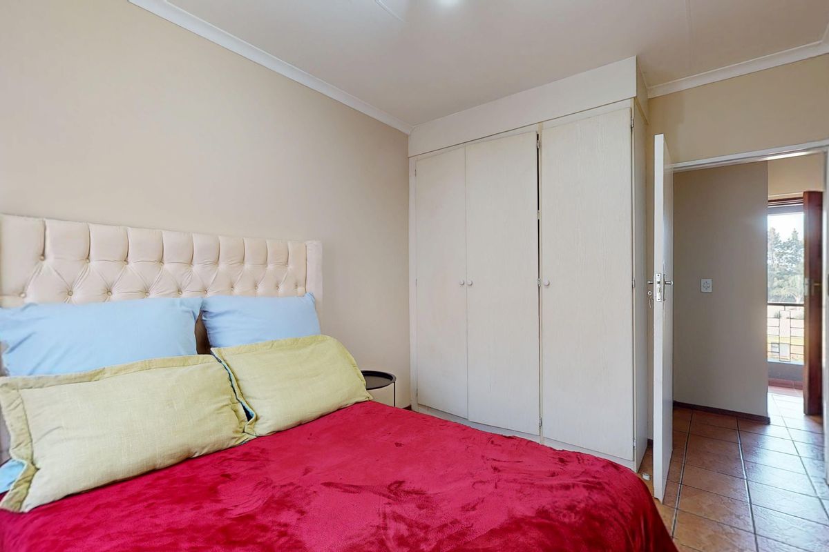 A bedroom featuring built-in wardrobes, tiled flooring, and neutral wall finishes, with an adjacent doorway leading to a balcony area.