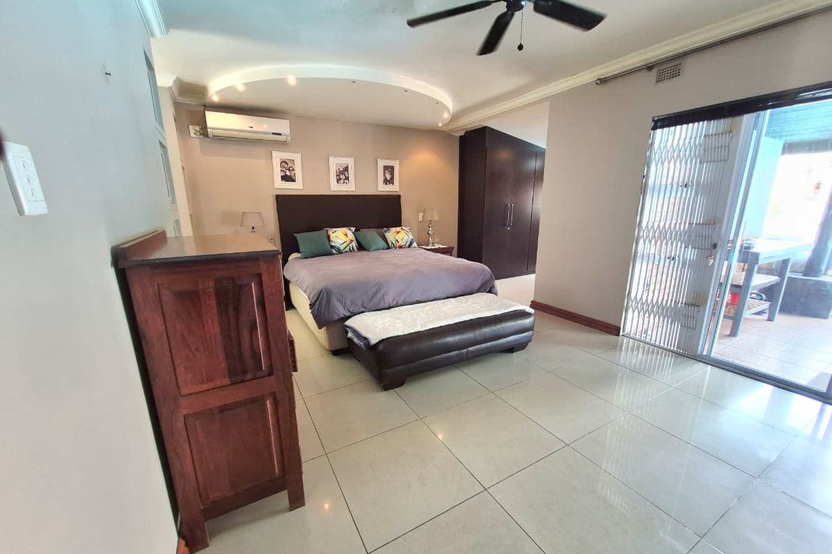 Spacious bedroom featuring tiled flooring, built-in cupboards, a ceiling fan, air conditioning, and direct access to an outdoor patio through sliding glass doors.