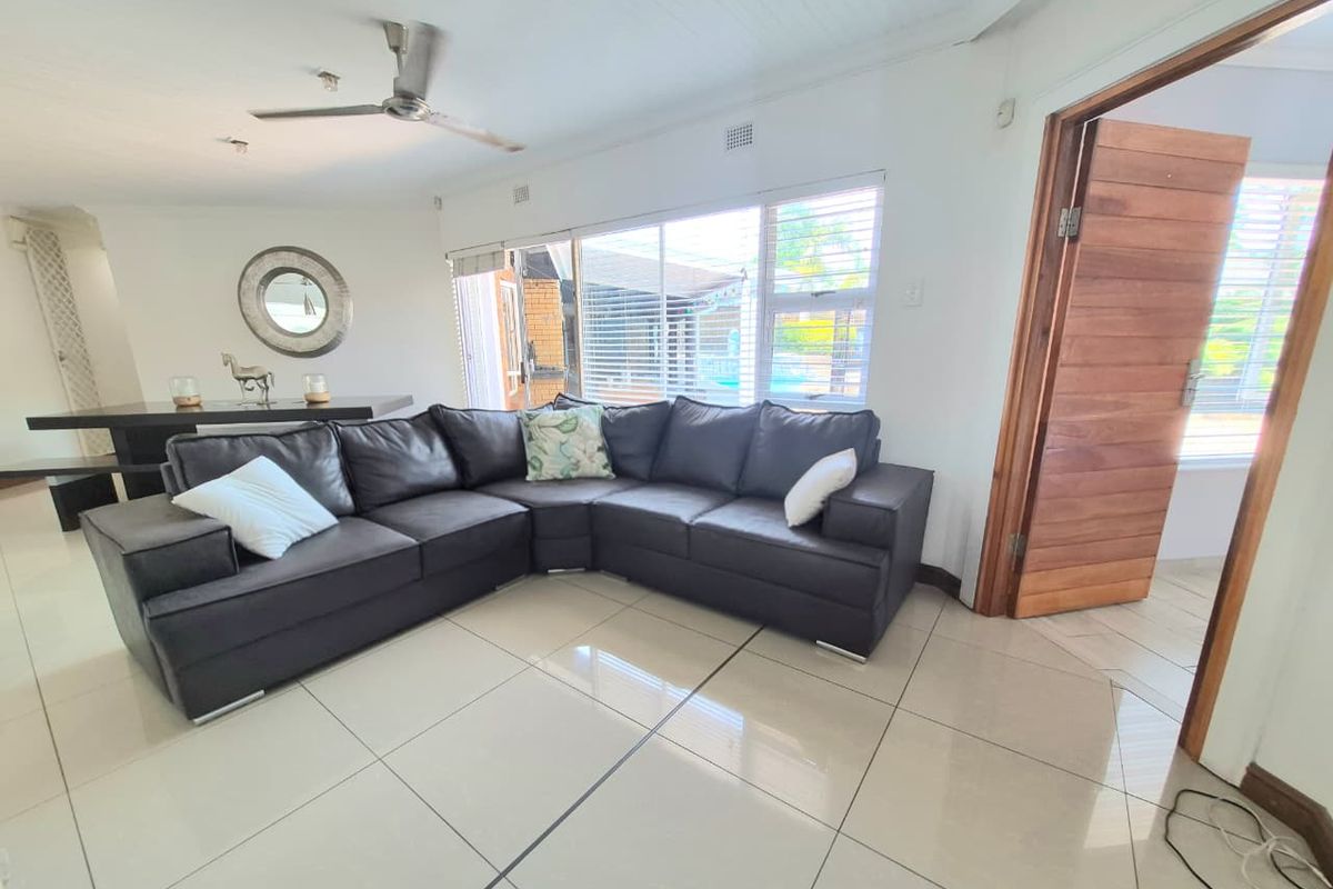 A bright living room featuring large format floor tiles, a ceiling fan, and direct access to the outdoor area through a wooden door.