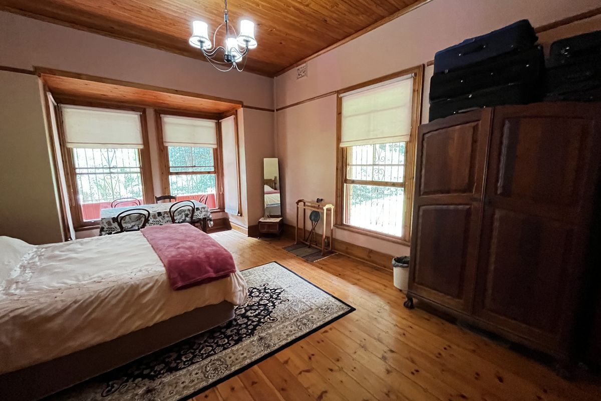 Spacious bedroom featuring polished timber flooring, a high timber-paneled ceiling, and large bay windows with security bars.