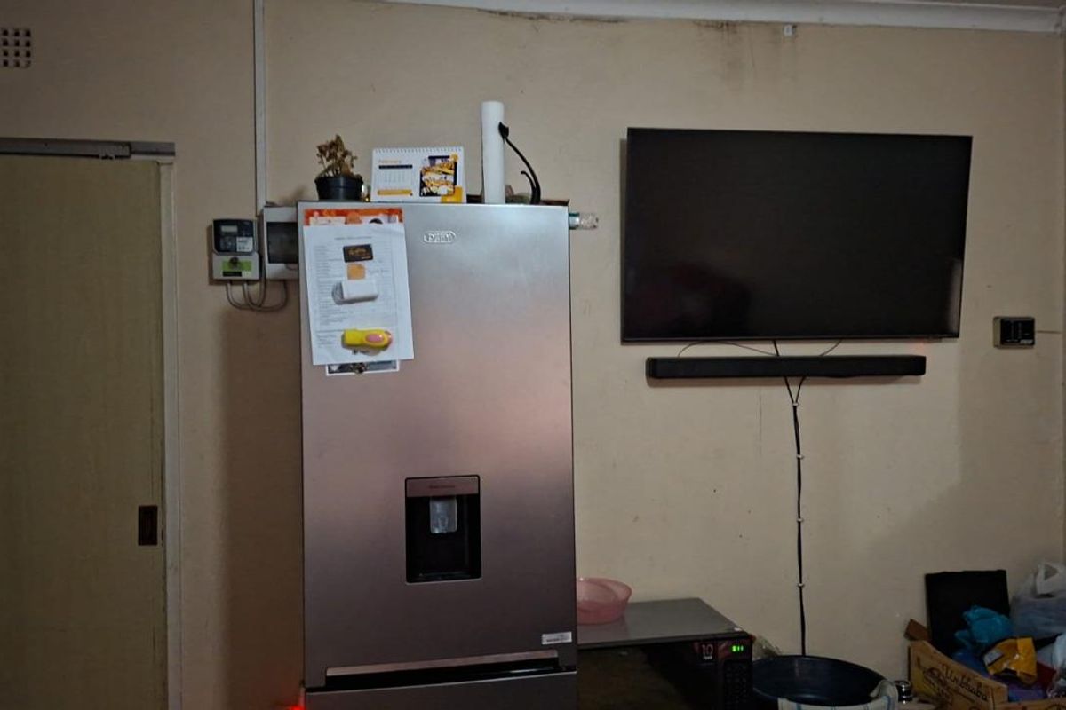 A living area featuring a wall-mounted television, soundbar, and space for a refrigerator, showing signs of wear and dated finishes.