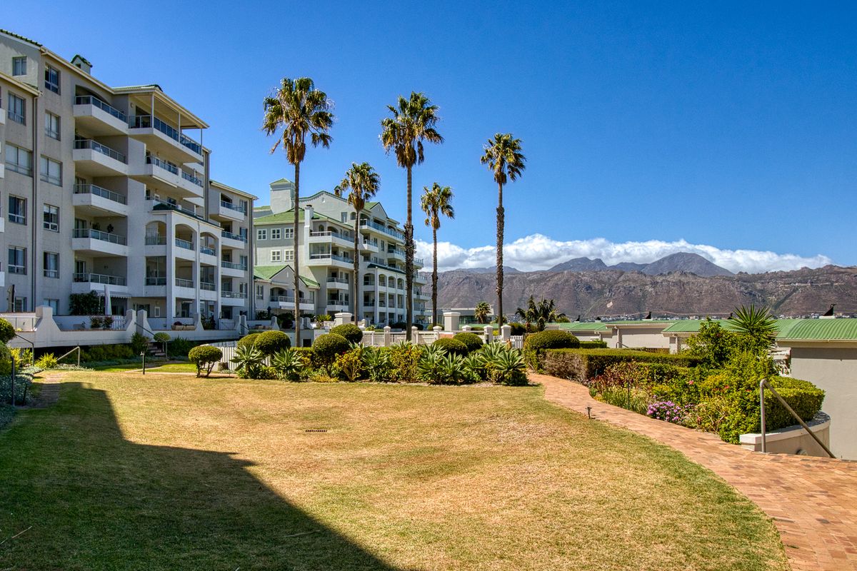 A well-maintained apartment complex exterior featuring landscaped gardens, paved walkways, and scenic mountain views.