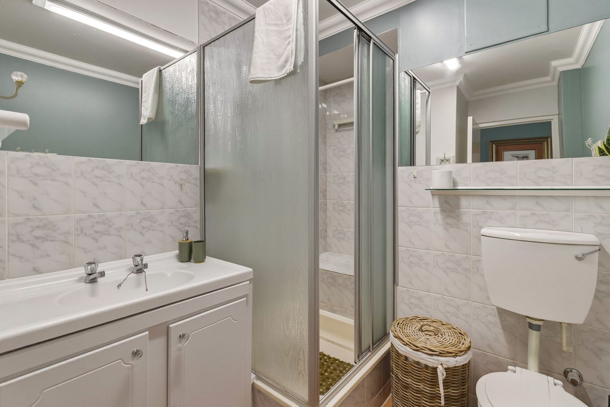 A functional bathroom featuring a vanity with integrated basin, a glass-enclosed shower, and a standard toilet with tiled walls.