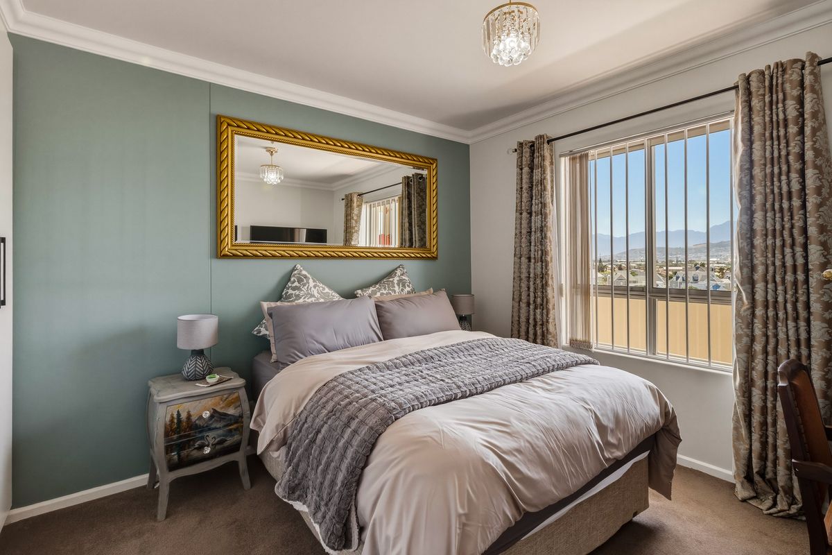 A well-maintained bedroom featuring a feature wall, crown molding, and a large window with security bars offering scenic mountain views.