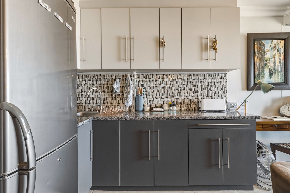 A compact, modern kitchen featuring two-tone cabinetry, granite countertops, and a decorative mosaic tile backsplash.