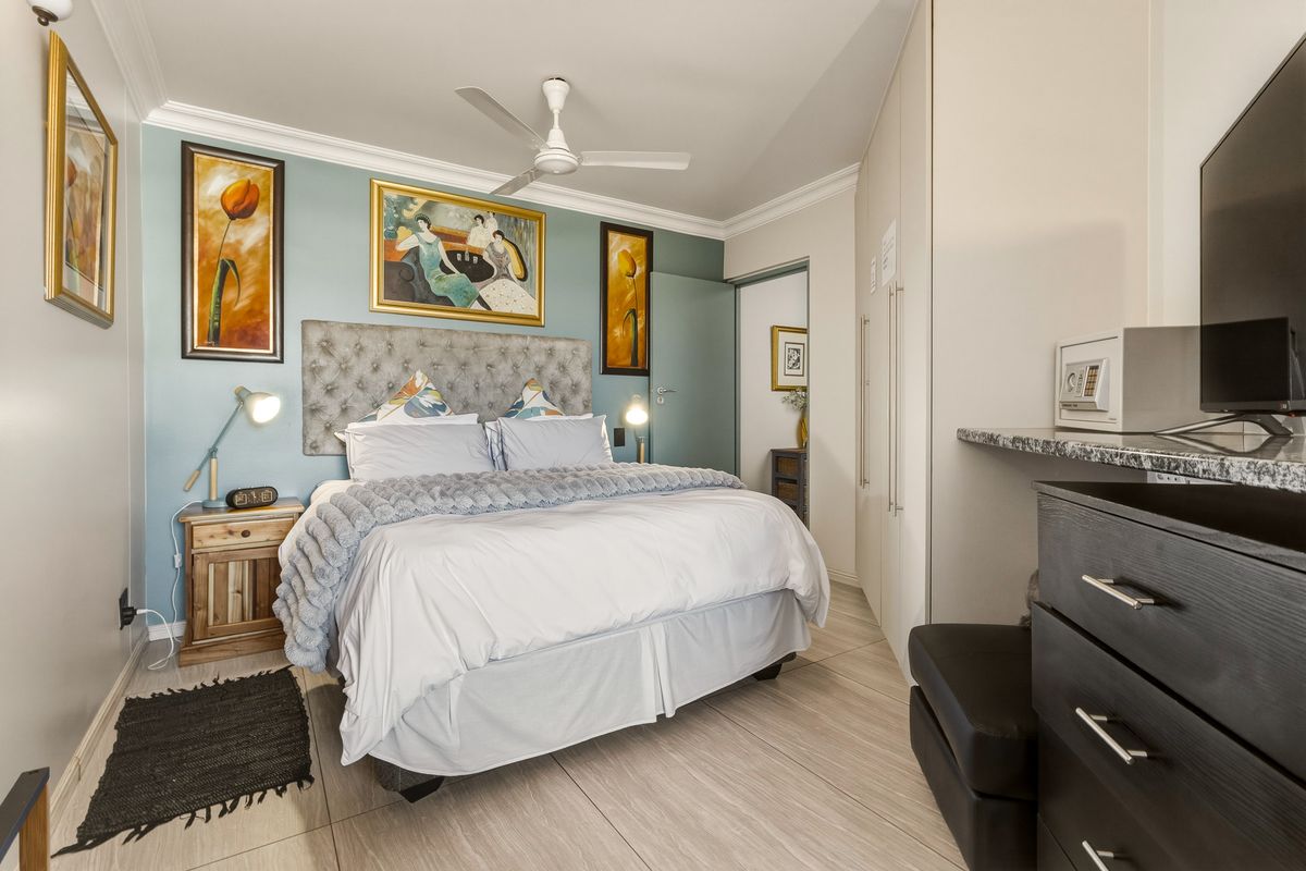 A well-maintained bedroom featuring built-in cupboards, a ceiling fan, tiled flooring, and a granite-topped vanity area.