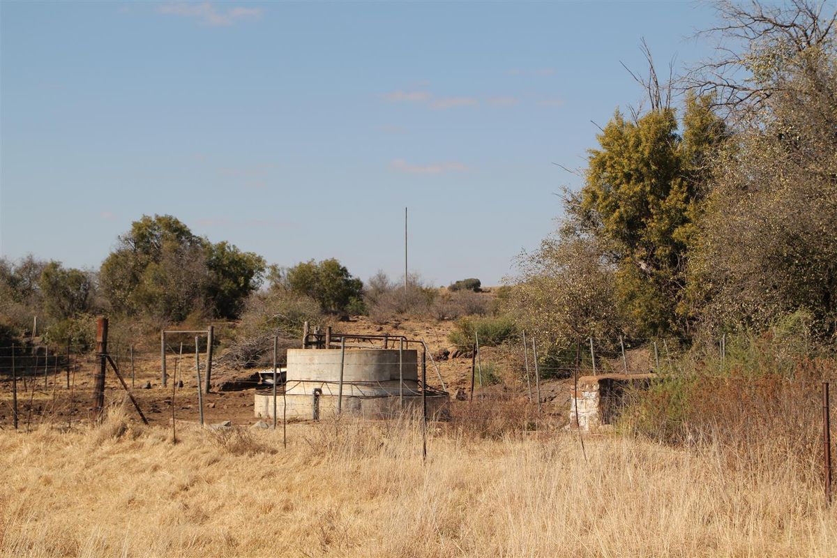 A view of a concrete water reservoir or well structure situated within a rural farm landscape with surrounding wire fencing.