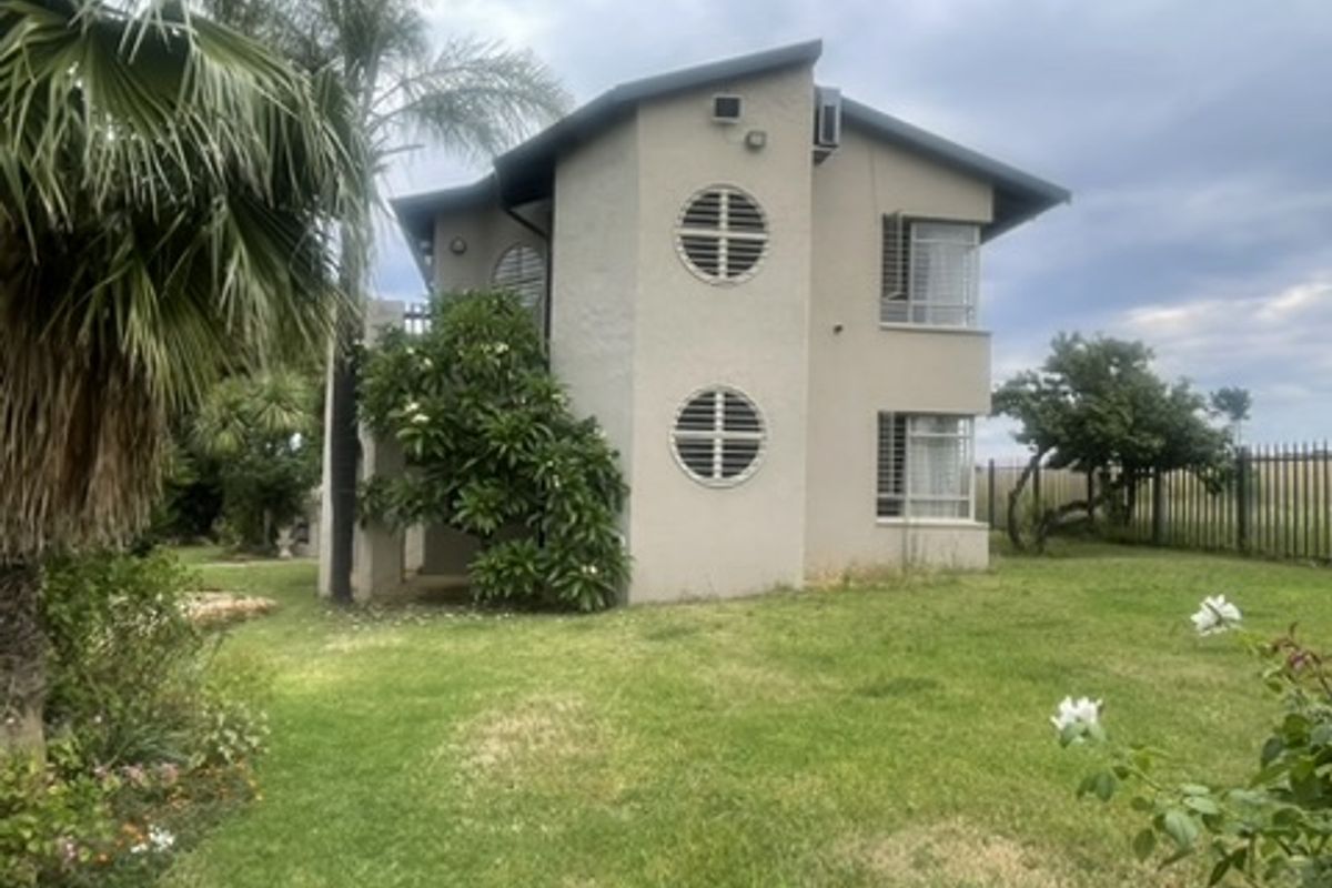 Rear view of a two-story residential building featuring circular windows, security bars, and a well-maintained garden area.