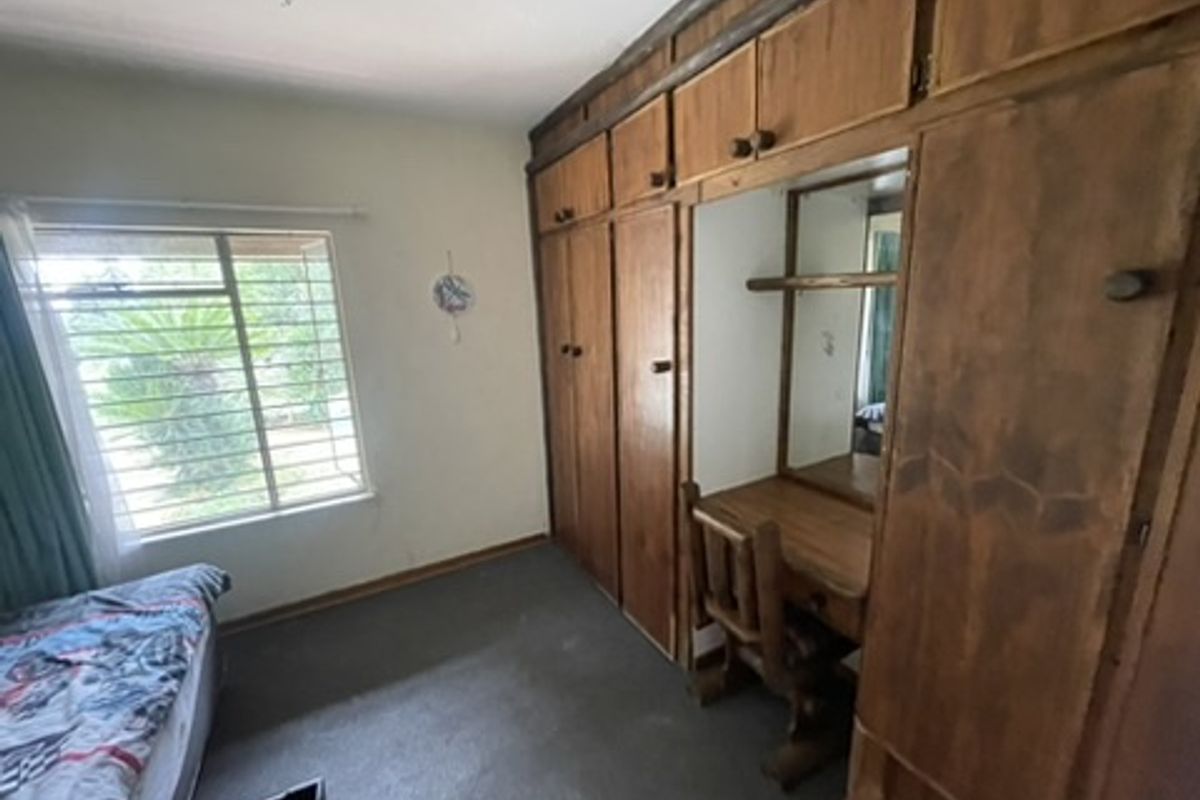 A bedroom featuring extensive built-in wooden cabinetry and a vanity unit, with large windows fitted with security bars.