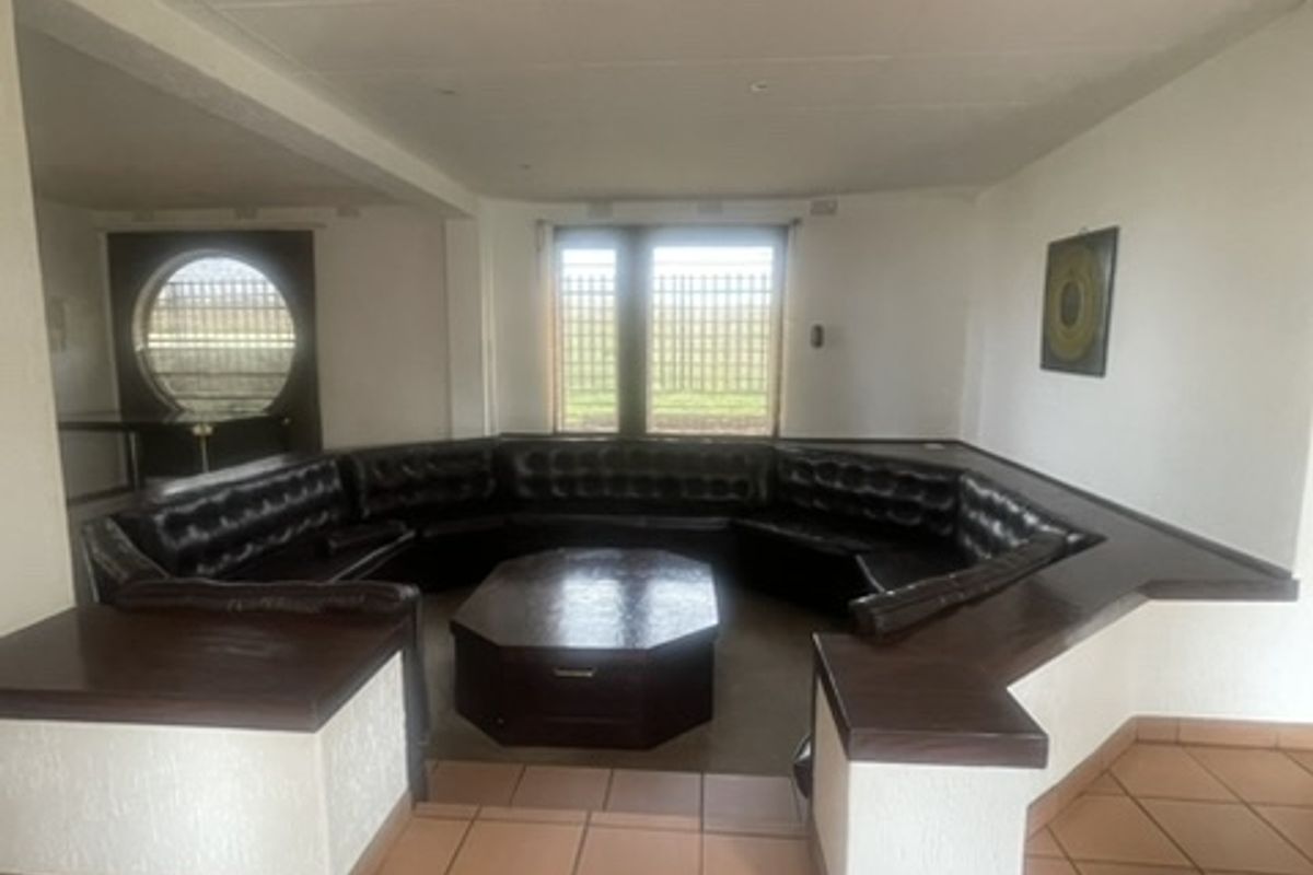 Spacious living area featuring a unique built-in sunken seating arrangement, tiled flooring, and large windows with security bars.