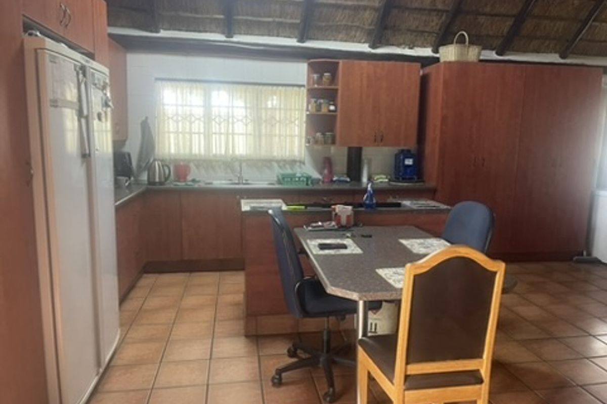 A kitchen featuring wooden cabinetry, tiled flooring, and a traditional thatched ceiling, offering a rustic aesthetic with functional workspace and an integrated island.