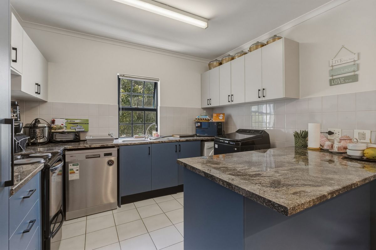 A functional kitchen featuring granite countertops, tiled splashbacks, white upper cabinetry, and blue lower cabinetry with integrated appliance space.