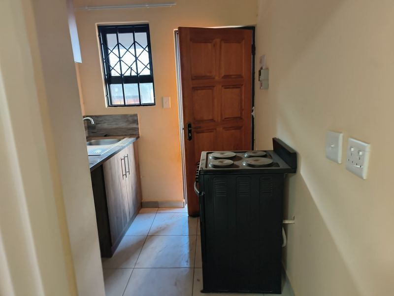 Compact kitchen featuring built-in cabinetry, a stainless steel sink, tiled flooring, and a freestanding stove with direct access to the exterior.