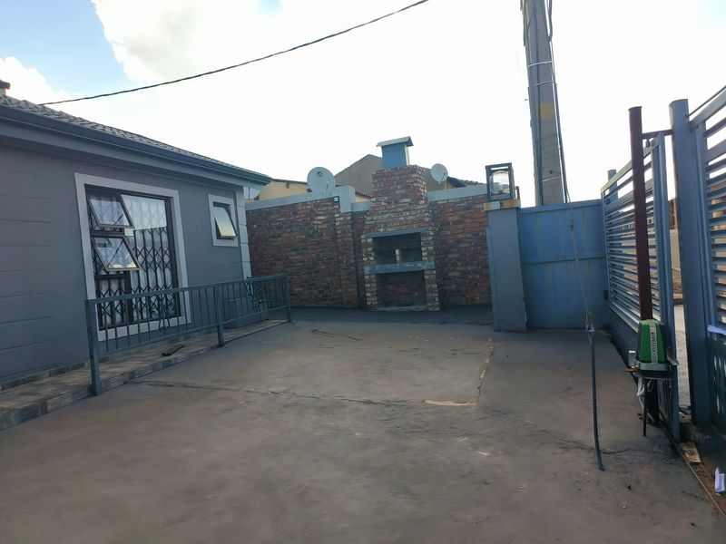 Rear courtyard area featuring a built-in brick braai, paved flooring, and secure gated access.