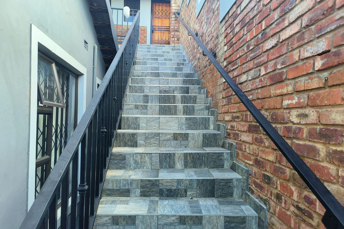An exterior staircase featuring tiled steps, a metal handrail, and an exposed brick wall leading to an entrance with a security gate.