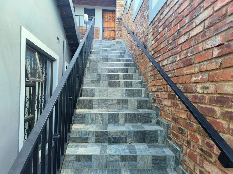 An exterior staircase featuring tiled steps, a metal handrail, and an exposed brick wall leading to an entrance with a security gate.