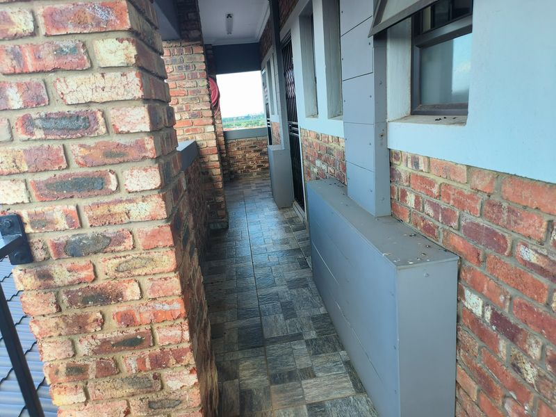 A covered balcony area featuring exposed brick walls, tiled flooring, and a security gate, offering a functional outdoor space.